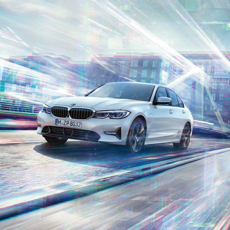 BMW 3-serie Sedan 330e på farten. BMW 3-serie Sedan 330e som kjører foran bylandskap.