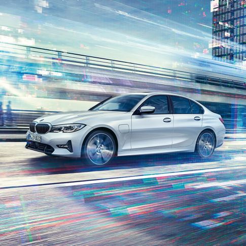 BMW 3-serie Sedan 330e på farten, sett fra siden. BMW 3-serie Sedan 330e som kjører foran bylandskap, sett fra siden.