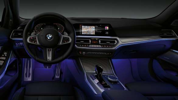 BMW 3-serie Sedan (G20), omgivelseslys. Førerplassen i BMW 3-serie Sedan (G20) med fotrommet belyst av blå bakgrunnsbelysning sett forfra.