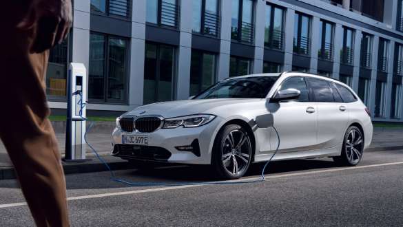 Plug-in hybrid BMW 3-serie Touring 2021 G21 sett på skrå forfra ved lading Plug-in hybrid BMW 3-serie Touring 2021 G21 sett på skrå forfra ved lading foran en bygning