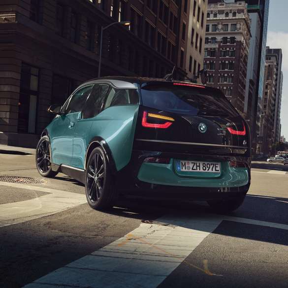 BMW i3 2018 sett skrått bakfra kjørende BMW i3 I01 2018 Jucarobeige med detaljer i frostgrå metallic sett skrått bakfra kjørende i bylandskap