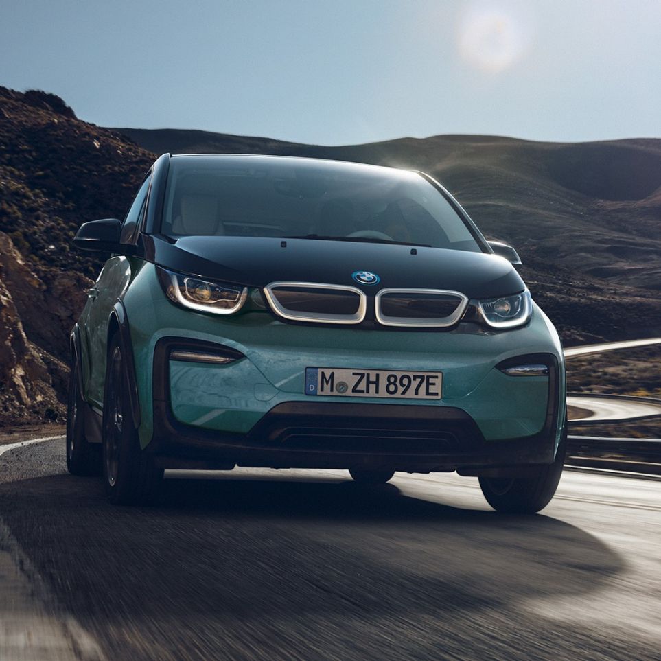 BMW i3 2018 sett fra siden kjørende BMW i3 I01 2018 Jucarobeige med detaljer i frostgrå metallic sett fra siden kjørende i bylandskap