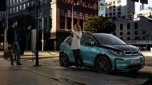 BMW i3 2018 ved en offentlig ladestasjon Jucarobeige med detaljer i frostgrå metallic Et par lader sin BMW i3 ved en offentlig ladestasjon I01 2018 Jucarobeige med detaljer i frostgrå metallic