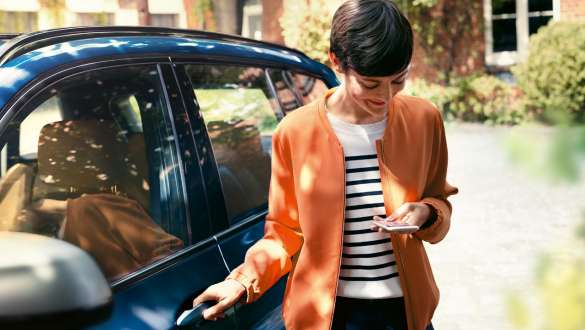 Kvinne ser på smarttelefonen sin og åpner døren til sin BMW BMW Teleservices kvinne ser på smarttelefonen sin og åpner døren til sin BMW