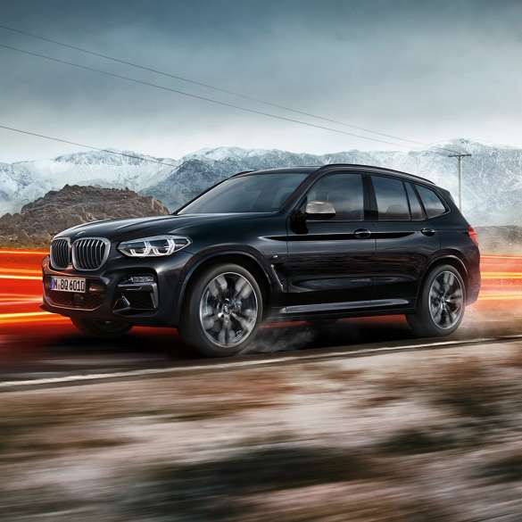 BMW X3 M40i og BMW X3 M40d sett fra siden. Utvendig design på BMW X3 M40i og BMW X3 M40d i safirsort metallic som kjører, sett fra siden i fjellandskap med lysstriper.