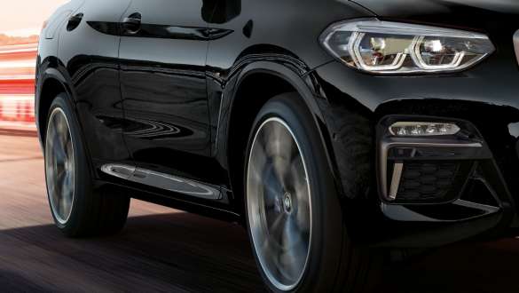 BMW X4 M40i og BMW X4 M40d sett skrått fra siden. Utvendig design på BMW X4 M40i og BMW X4 M40d i safirsort metallic som kjører, sett skrått fra siden med roterende lettmetallfelger.