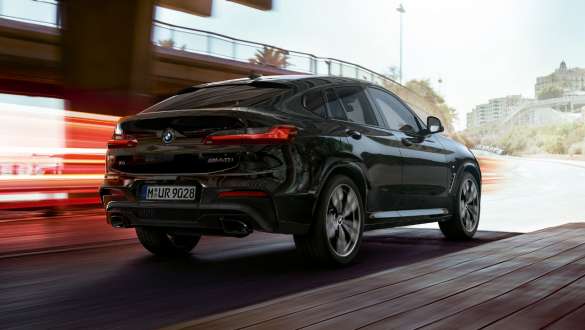 BMW X4 M40i sett skrått bakfra. Utvendig design på BMW X4 M40i i safirsort metallic som kjører, sett skrått bakfra med lysstriper.