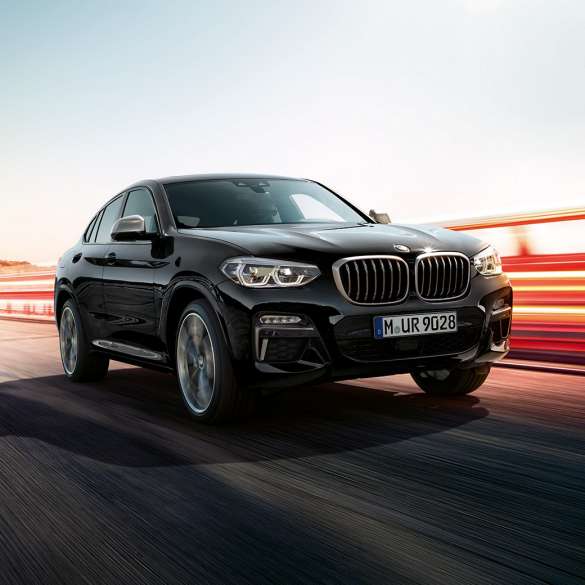 BMW X4 M40i sett skrått bakfra. Utvendig design på BMW X4 M40i i safirsort metallic som kjører, sett skrått bakfra med lysstriper.
