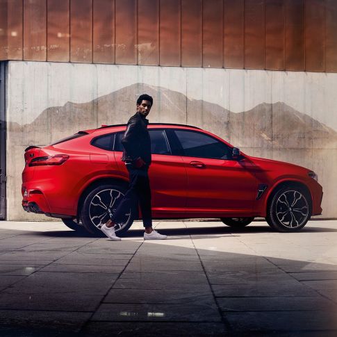 BMW X4 M Competition sett fra siden med ung mann. Utvendig design på BMW X4 M Competition i torontorød metallic med ung mann sett fra siden.
