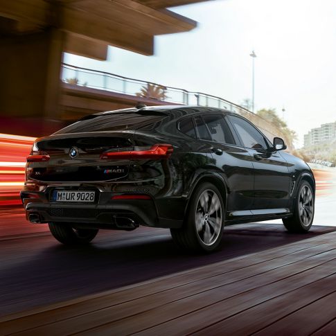 BMW X4 M40i sett skrått bakfra. Utvendig design på BMW X4 M40i i safirsort metallic, sett skrått fra høyre bak med lysstriper.