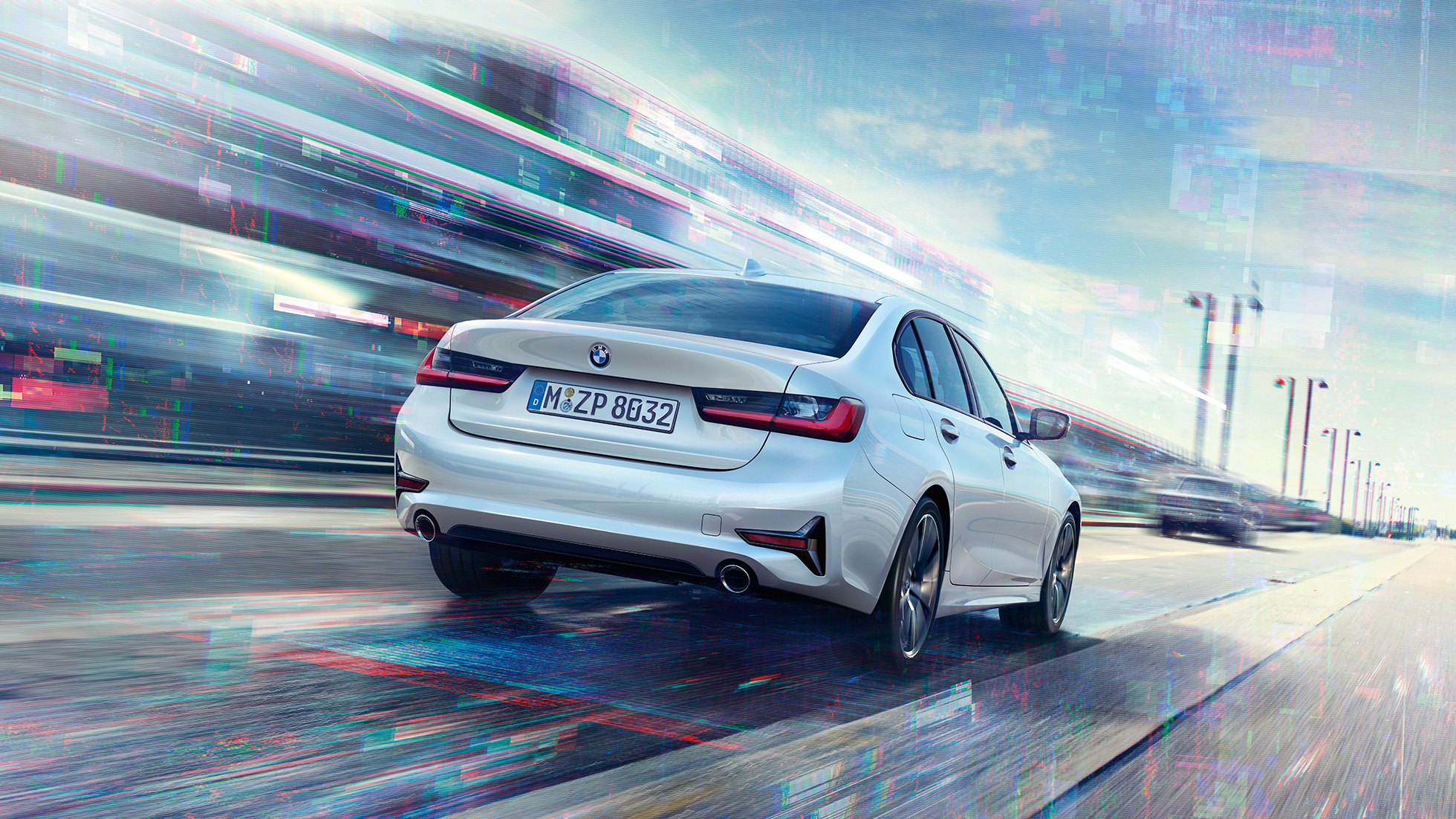 BMW 3-serie Sedan 330e sett bakfra. BMW 3-serie Sedan 330e som kjører foran bylandskap, sett skrått bakfra.