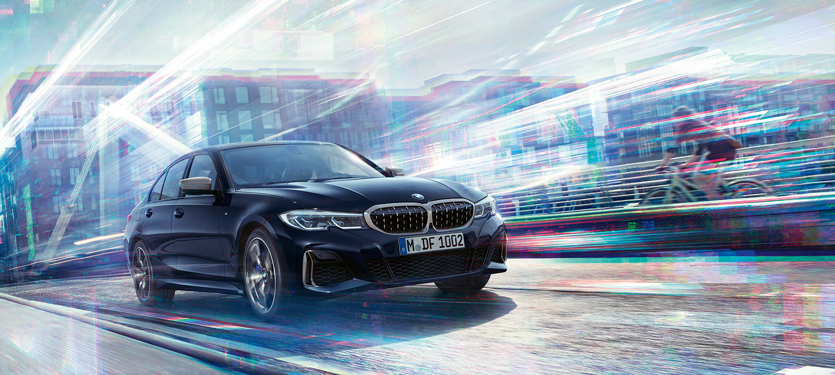BMW 3-serie Sedan, BMW M340i xDrive. BMW M340i xDrive som kjører på vei foran bylandskap, sett skrått bakfra.