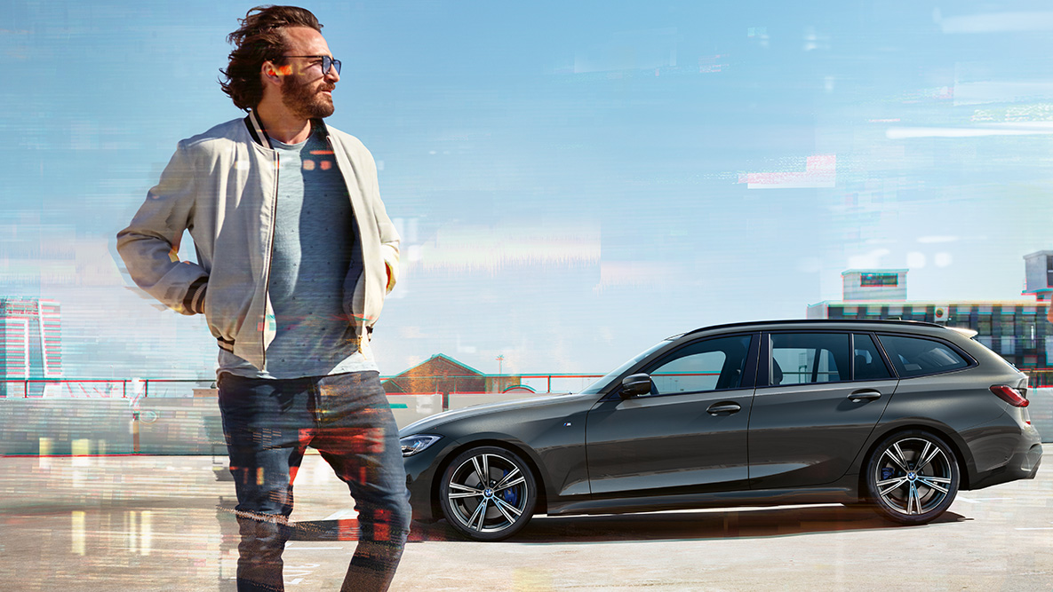 BMW 3-serie Touring (G21), design sett på skrå forfra BMW 3-serie Touring (G21) dravittgrå, sett på skrå forfra på vei over bro i landlige omgivelser