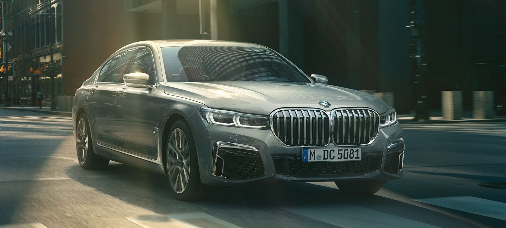 Grå BMW 7-serie Sedan som kjører, sett skrått forfra Grå BMW 7-serie Sedan som kjører i bylandskap, sett skrått forfra