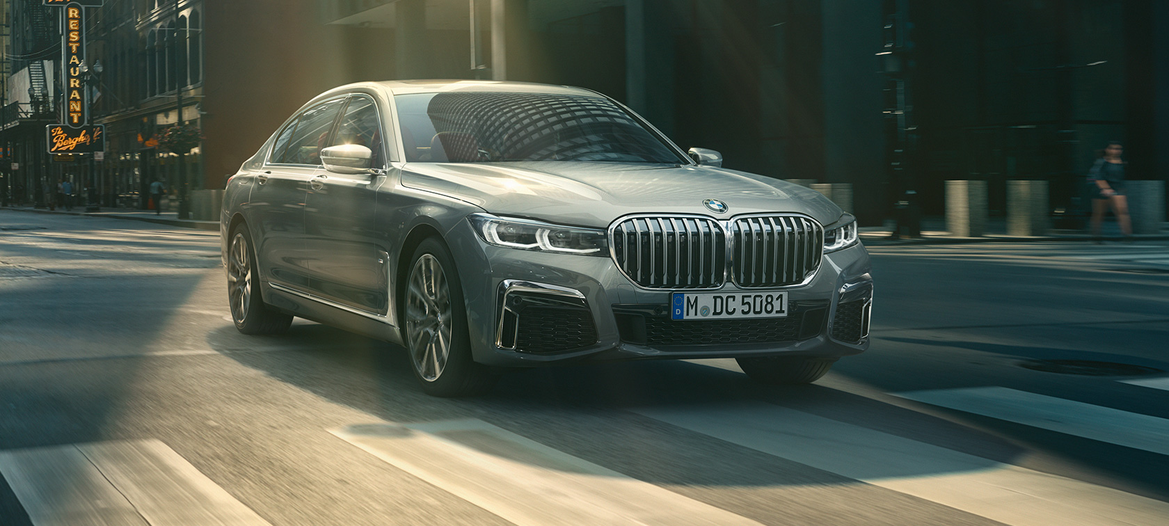 Grå BMW 7-serie Sedan som kjører, sett skrått forfra Grå BMW 7-serie Sedan som kjører i bylandskap, sett skrått forfra