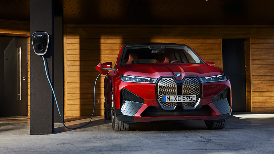 BMW iX i20 elektrisk SUV BMW iX xDrive50 Lading BMW iX i20 2021 elektrisk SUV BMW iX xDrive50 Aventurinrød lader ved en BMW Wallbox Lading