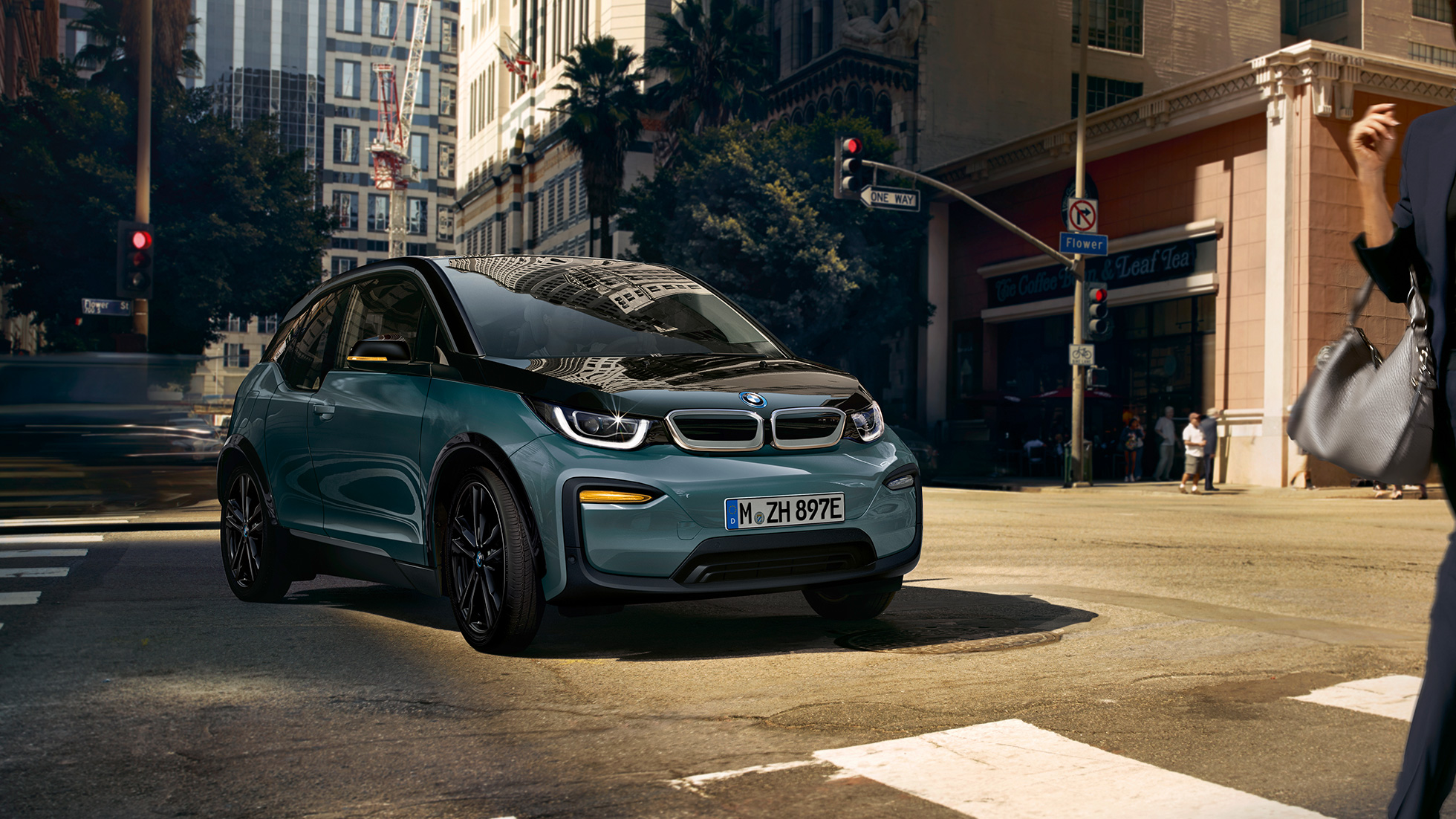 BMW i3 2018 sett skrått forfra kjørende BMW i3 I01 2018 Jucarobeige med detaljer i frostgrå metallic sett skrått forfra kjørende i bylandskap