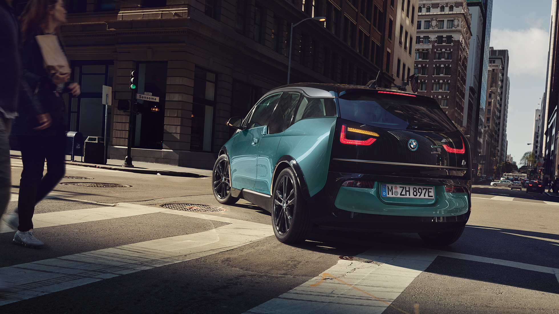BMW i3 2018 sett skrått bakfra kjørende BMW i3 I01 2018 Jucarobeige med detaljer i frostgrå metallic sett skrått bakfra kjørende i bylandskap