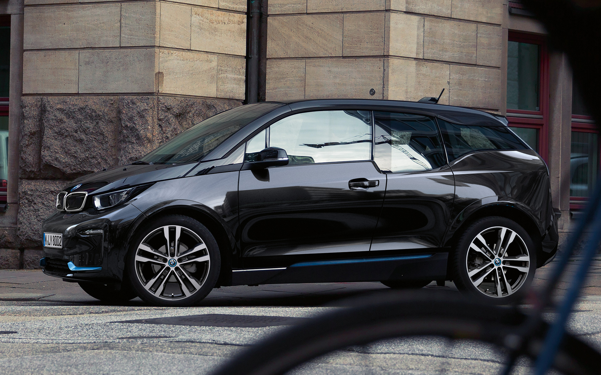 BMW i3s I01 2018 Fluid sort med detaljer i BMW i blått sett fra siden kjørende i bylandskap