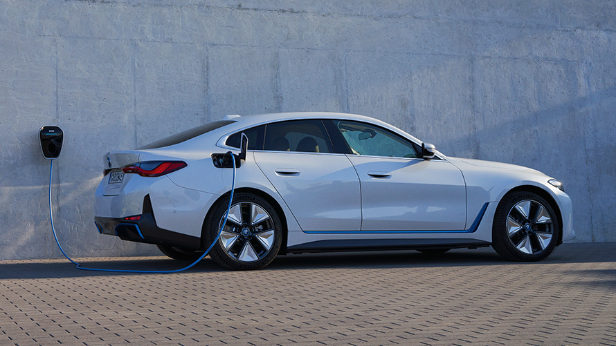 Sett fra siden med BMW Wallbox BMW i4 eDrive40 G26 2021 BMW i4 eDrive40 G26 2021 Mineralhvit Sett fra siden foran husvegg med BMW Wallbox ladestasjon