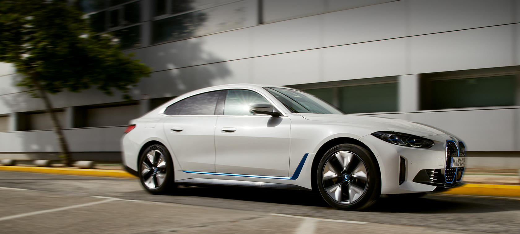 BMW i4 eDrive40 G26 2021 Sett skrått fra siden kjørende foran bygning BMW i4 eDrive40 G26 2021 Sett skrått fra siden kjørende foran bygning