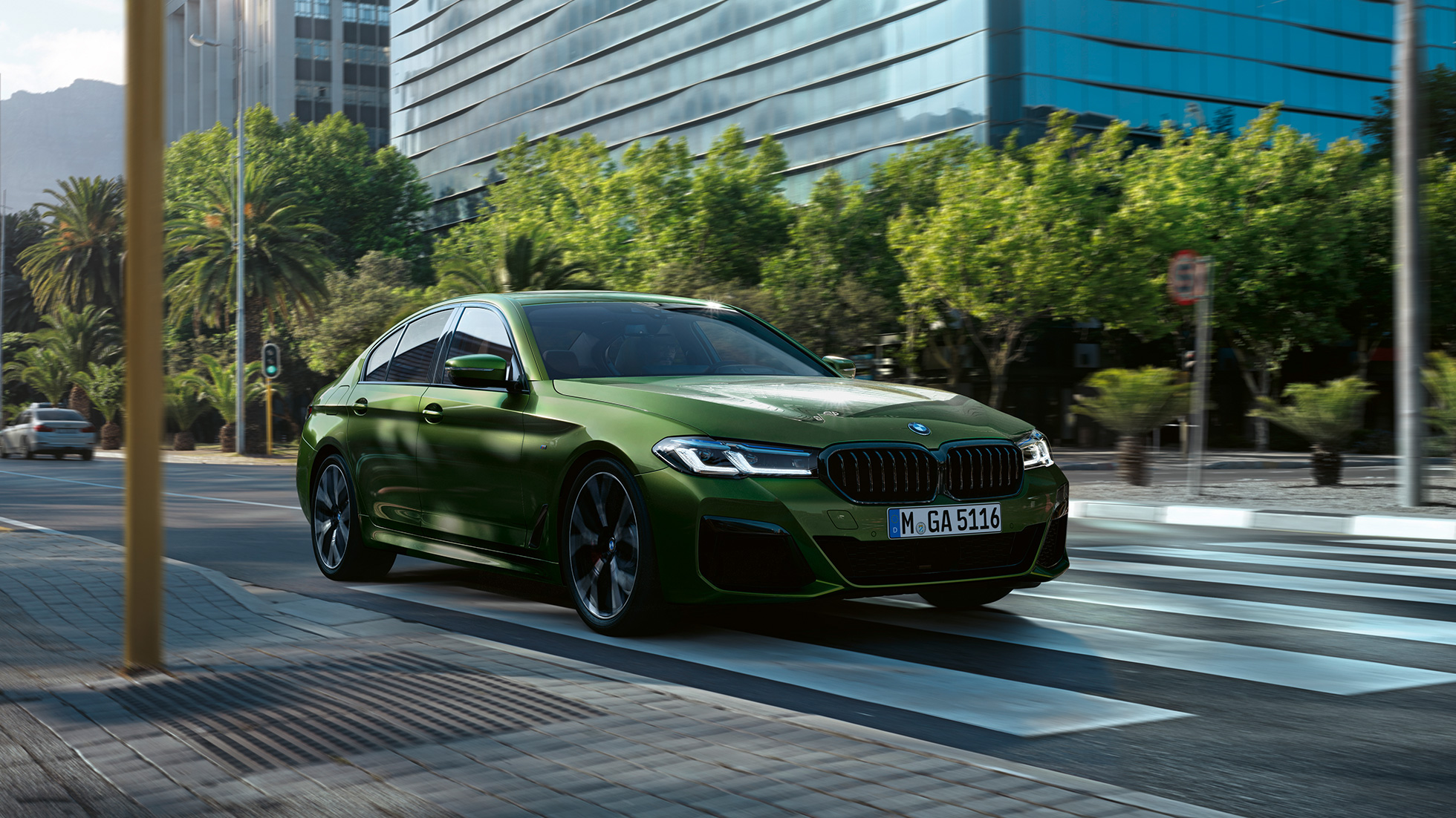 BMW M550i xDrive Sedan G30 LCI Facelift 2020 Sett skrått forfra kjørende BMW M5 Competition F90 LCI Facelift 2020 BMW Individual Verde Ermes grønn metallic Sett fra siden kjørende i byen