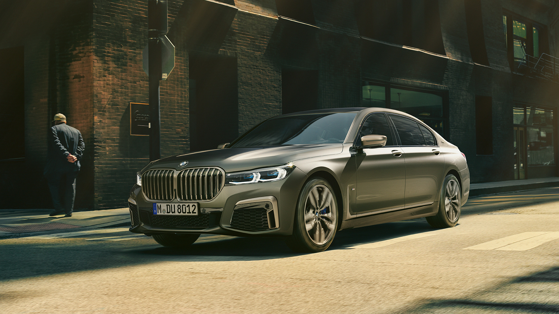 BMW M760Li xDrive sedan i bylandskap BMW M760Li xDrive sedan som kjører på en vei gjennom bylandskap, sett fra siden forfra