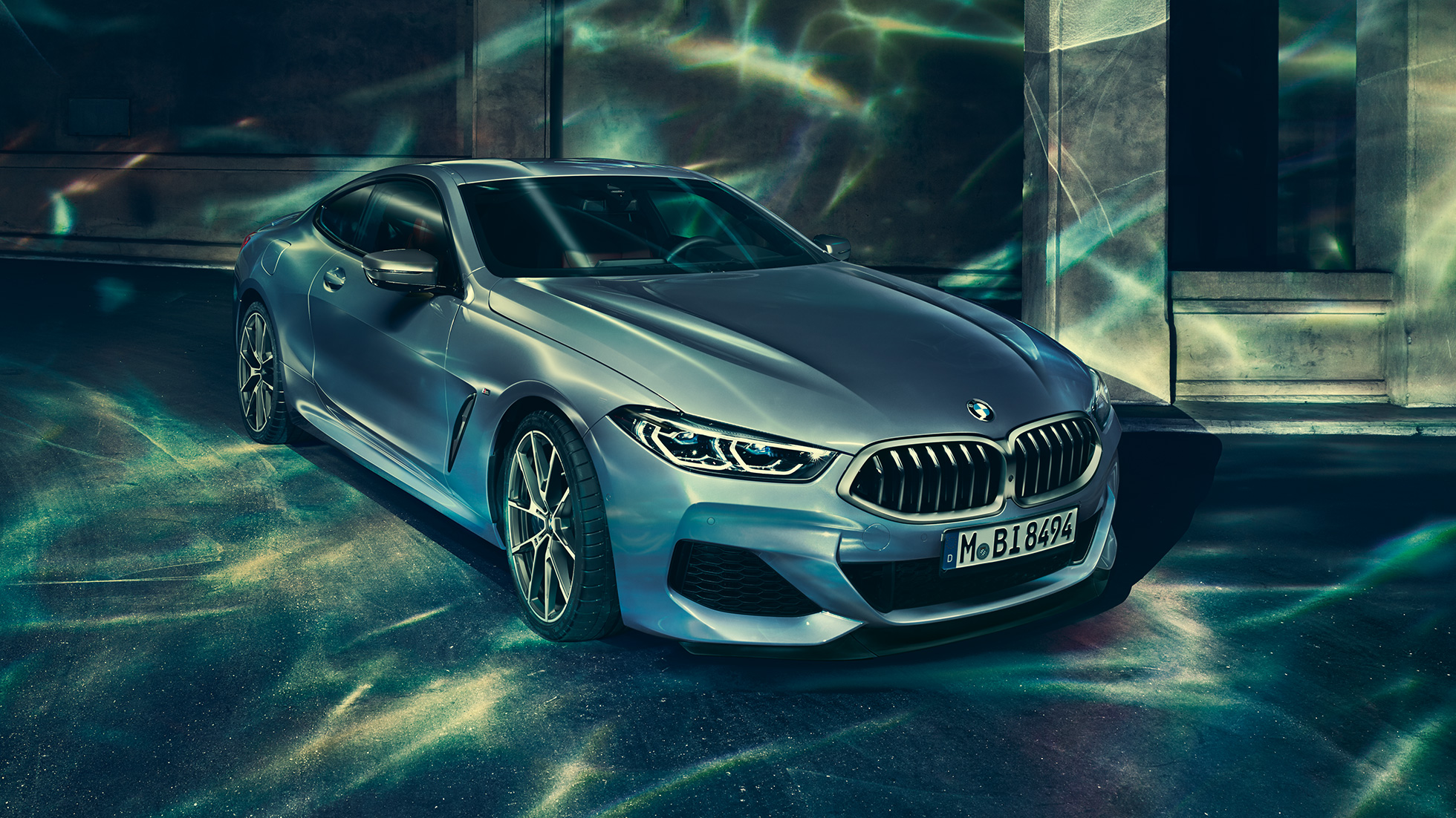 BMW M850i xDrive Coupé, sett skrått forfra fra venstre. BMW M850i xDrive Coupé i Barcelona blå metallic, sett skrått forfra fra venstre, stående foran bygning.