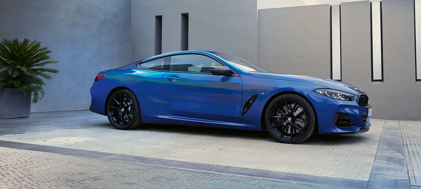 BMW M850i xDrive Coupé G15 LCI Facelift 2022 sett fra siden BMW M850i xDrive Coupé G15 LCI Facelift 2022 M Portimão-blå metallic sett fra siden foran en bygning