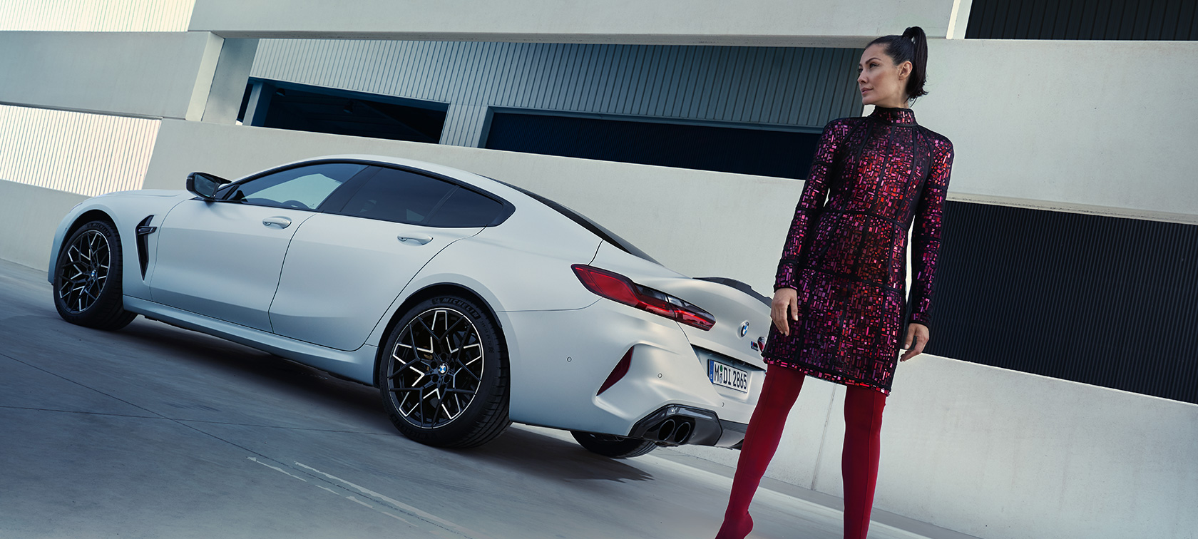 Sett på skrått bakfra BMW M8 Competition Gran Coupé F93 LCI 2022 BMW M8 Competition Gran Coupé F93 LCI Facelift 2022 BMW Individual Frozen Brilliant White metallic sett på skrått bakfra med kvinnelig modell ved siden av kjøretøyet
