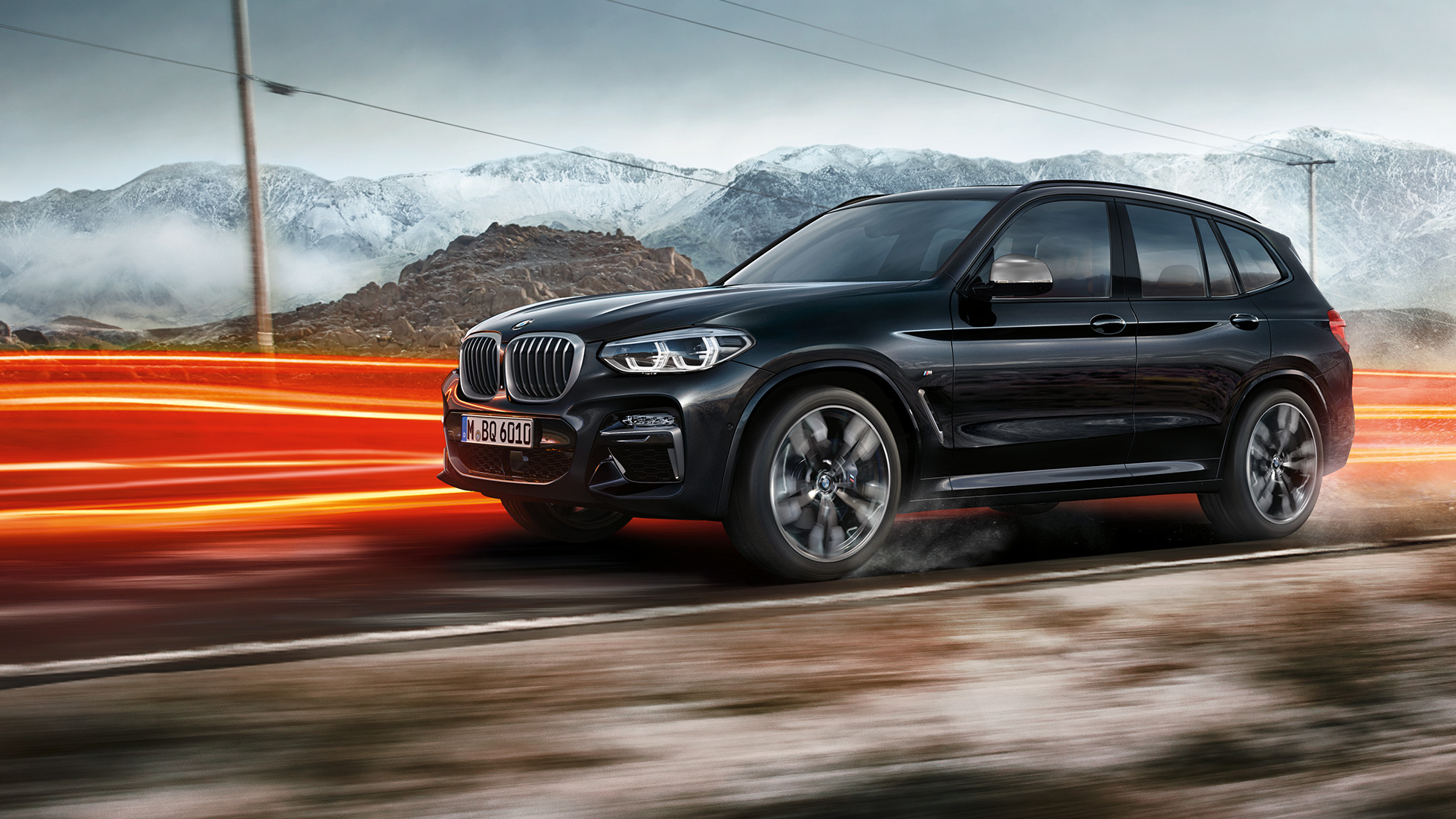 BMW X3 M40i og BMW X3 M40d sett fra siden. Utvendig design på BMW X3 M40i og BMW X3 M40d i safirsort metallic som kjører, sett fra siden i fjellandskap med lysstriper.
