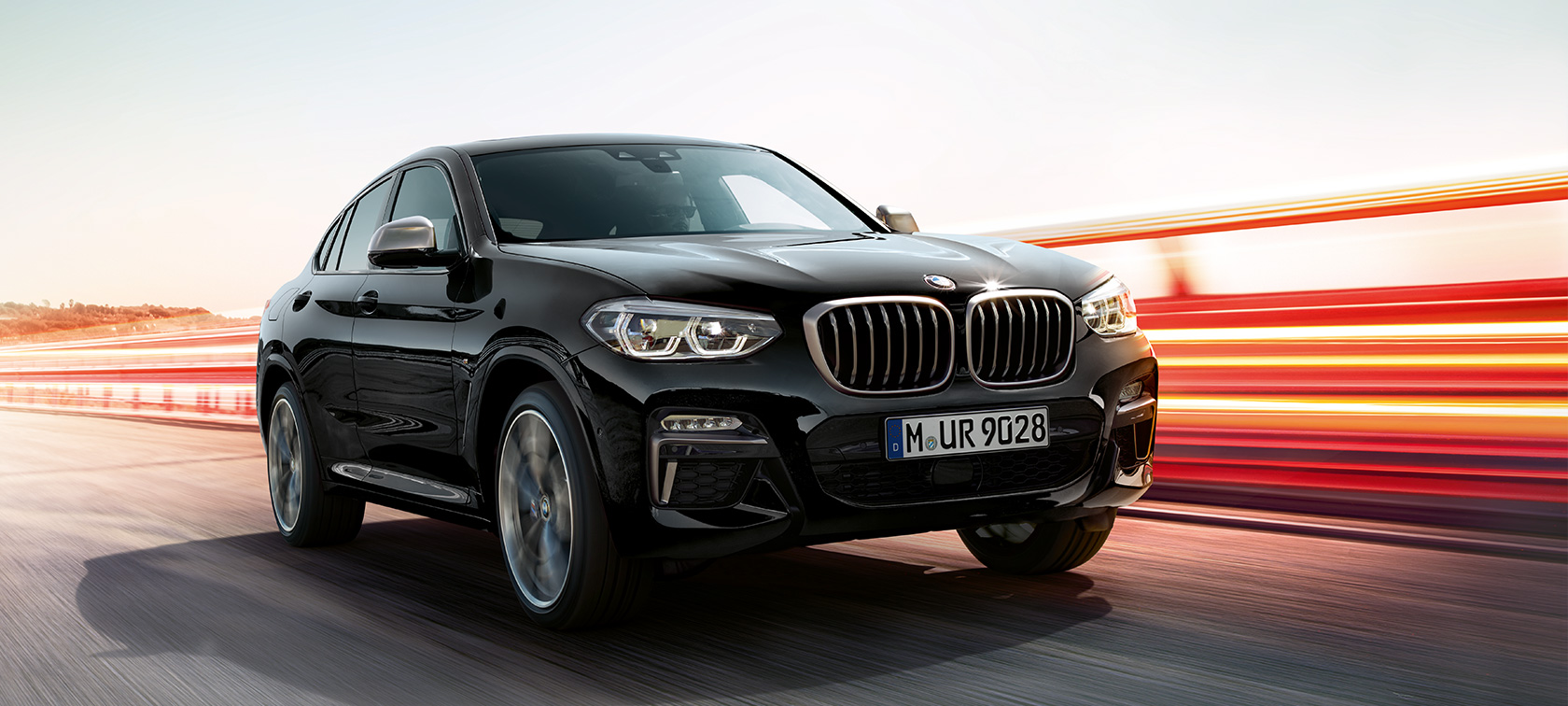 BMW X4 M40i og BMW X4 M40d sett skrått forfra fra venstre. Utvendig design på BMW X4 M40i og BMW X4 M40d i safirsort metallic som kjører, sett skrått fra venstre foran med lysstriper.