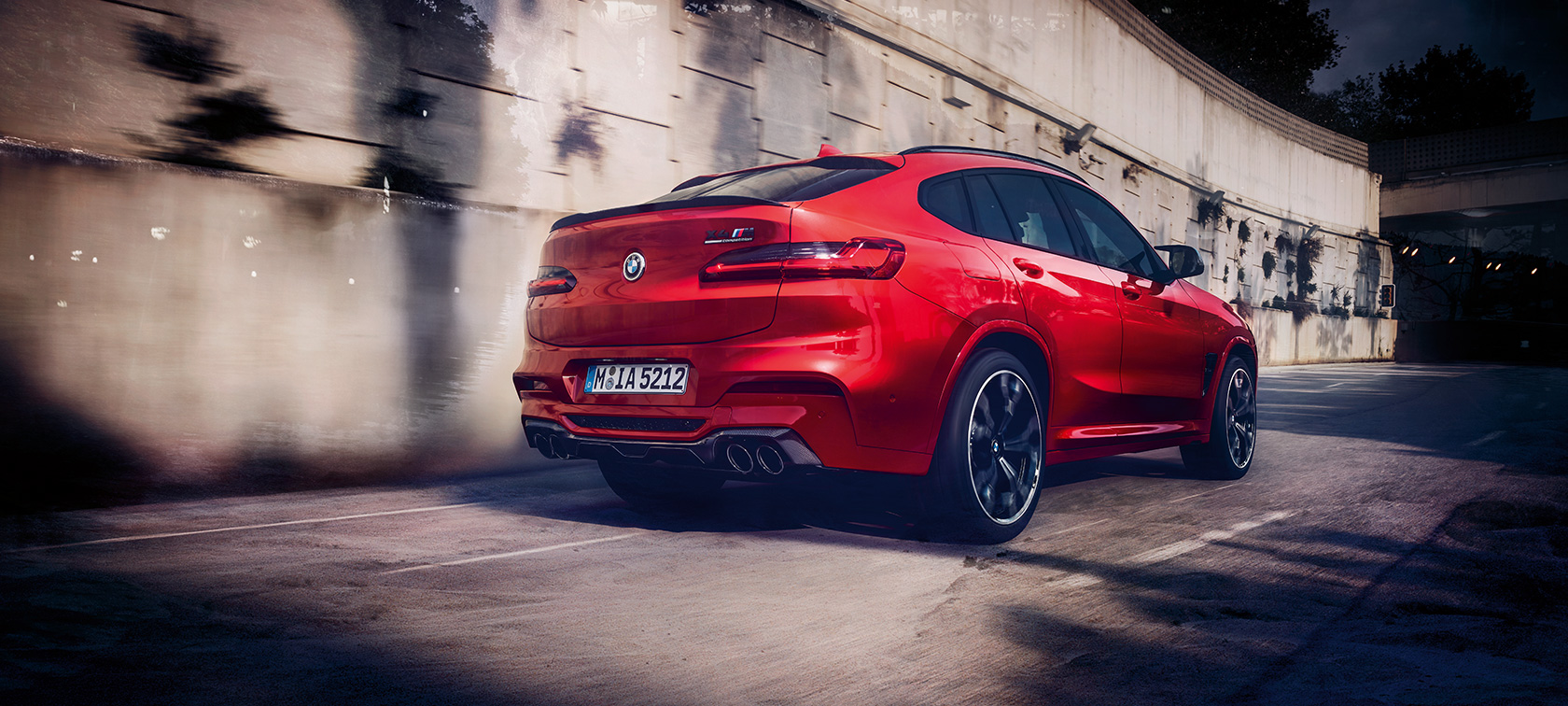 BMW X4 M Competition sett skrått bakfra. Utvendig design på BMW X4 M Competition i torontorød metallic som kjører, sett skrått bakfra.