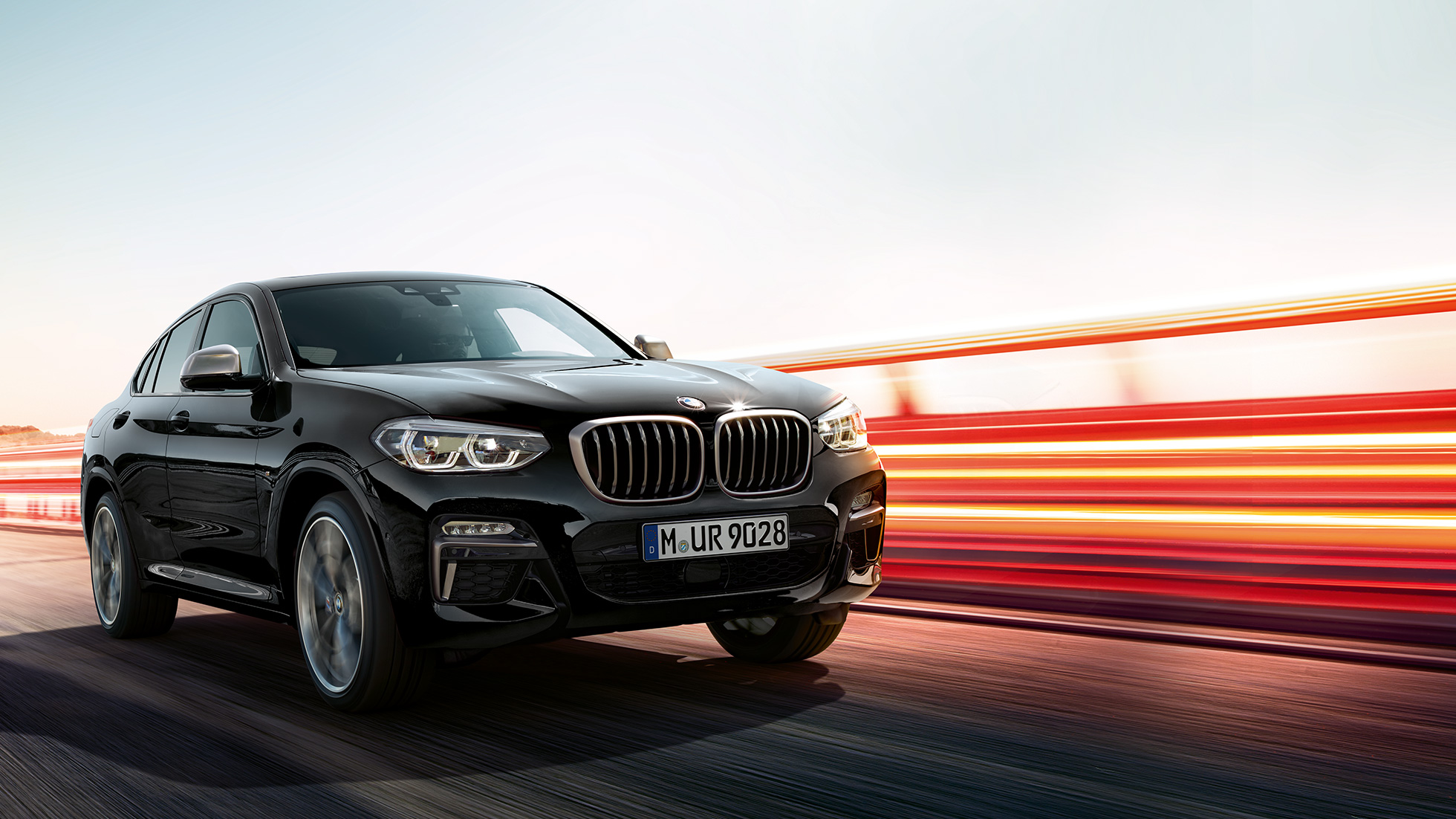BMW X4 M40i sett skrått bakfra. Utvendig design på BMW X4 M40i i safirsort metallic som kjører, sett skrått bakfra med lysstriper.