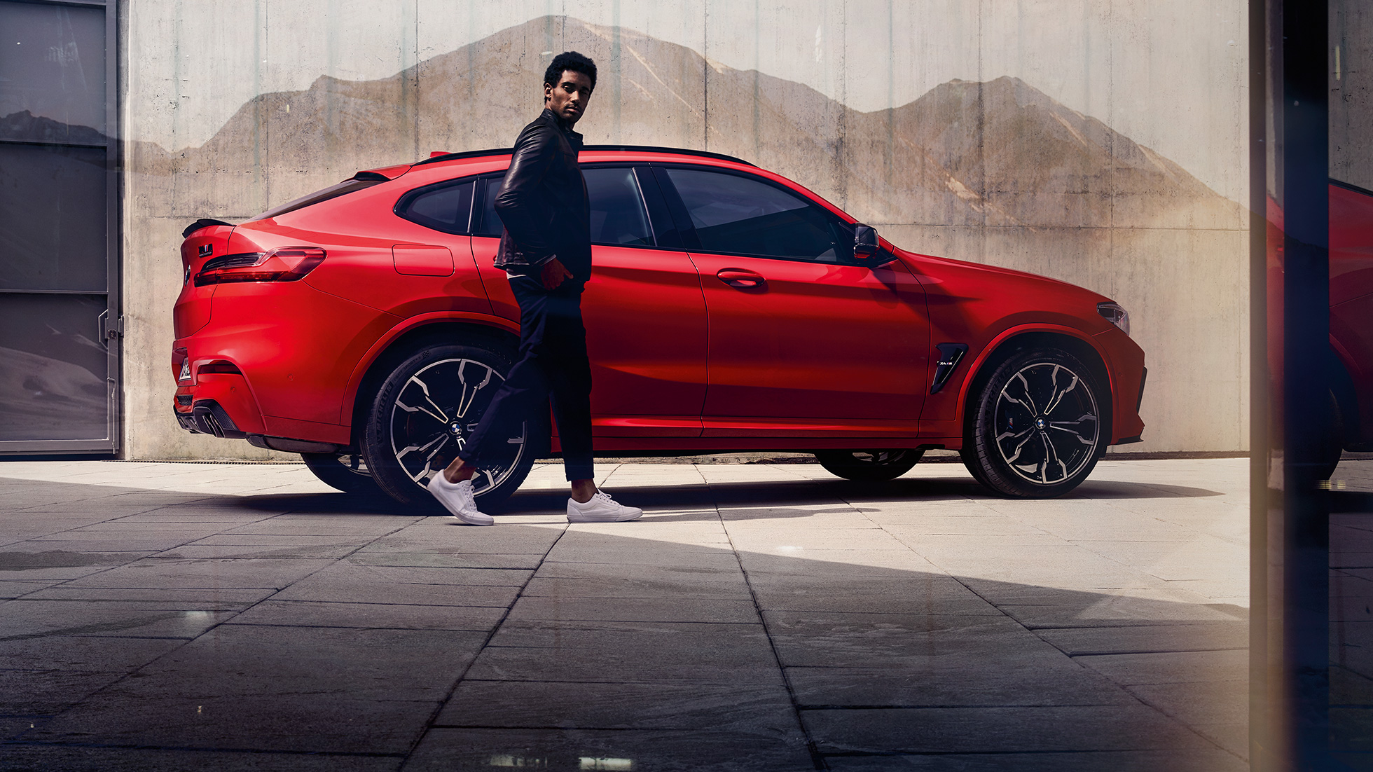 BMW X4 M Competition sett fra siden med ung mann. Utvendig design på BMW X4 M Competition i torontorød metallic med ung mann sett fra siden.