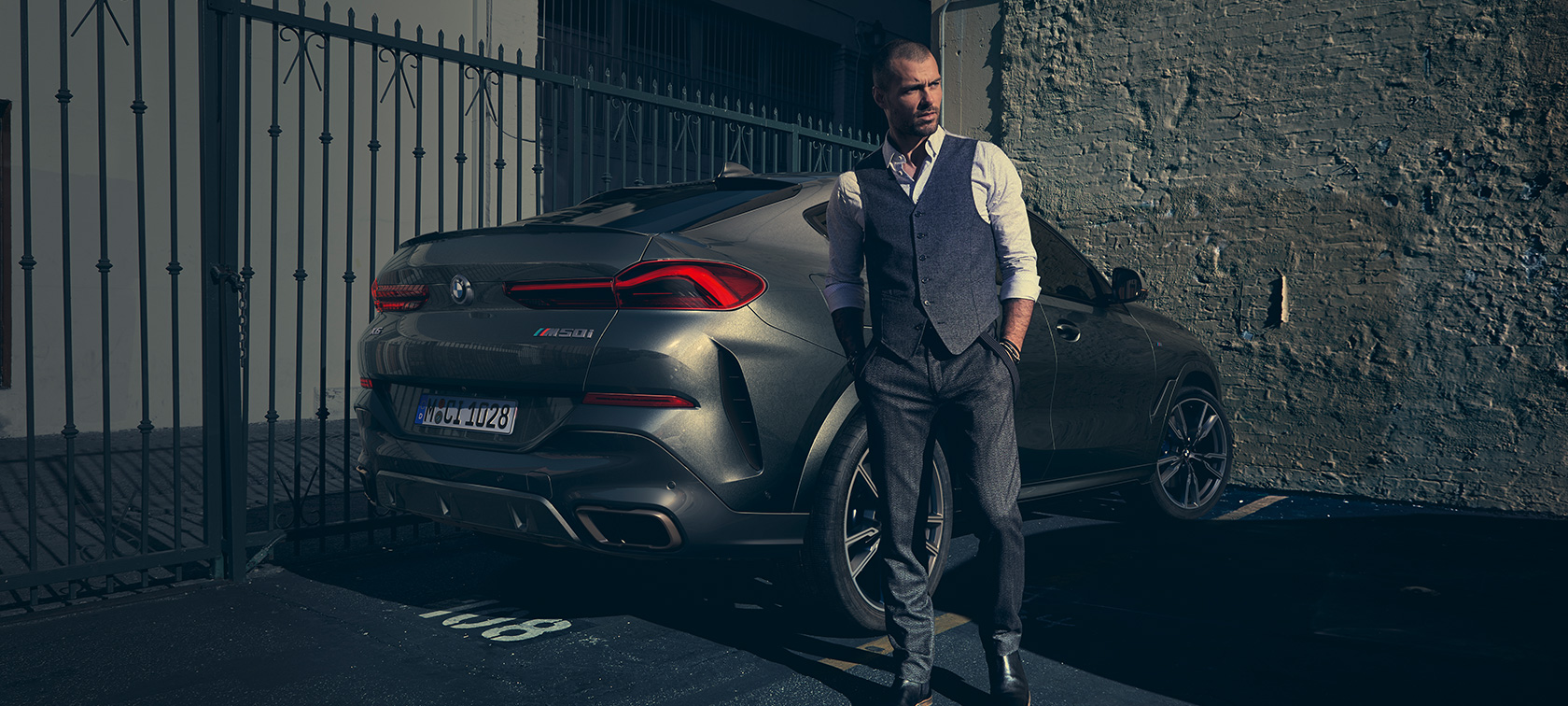 BMW X6 M50i sett skrått bakfra G06 Mann står ved siden av BMW X6 M50i G06 2018 SUV sett skrått bakfra