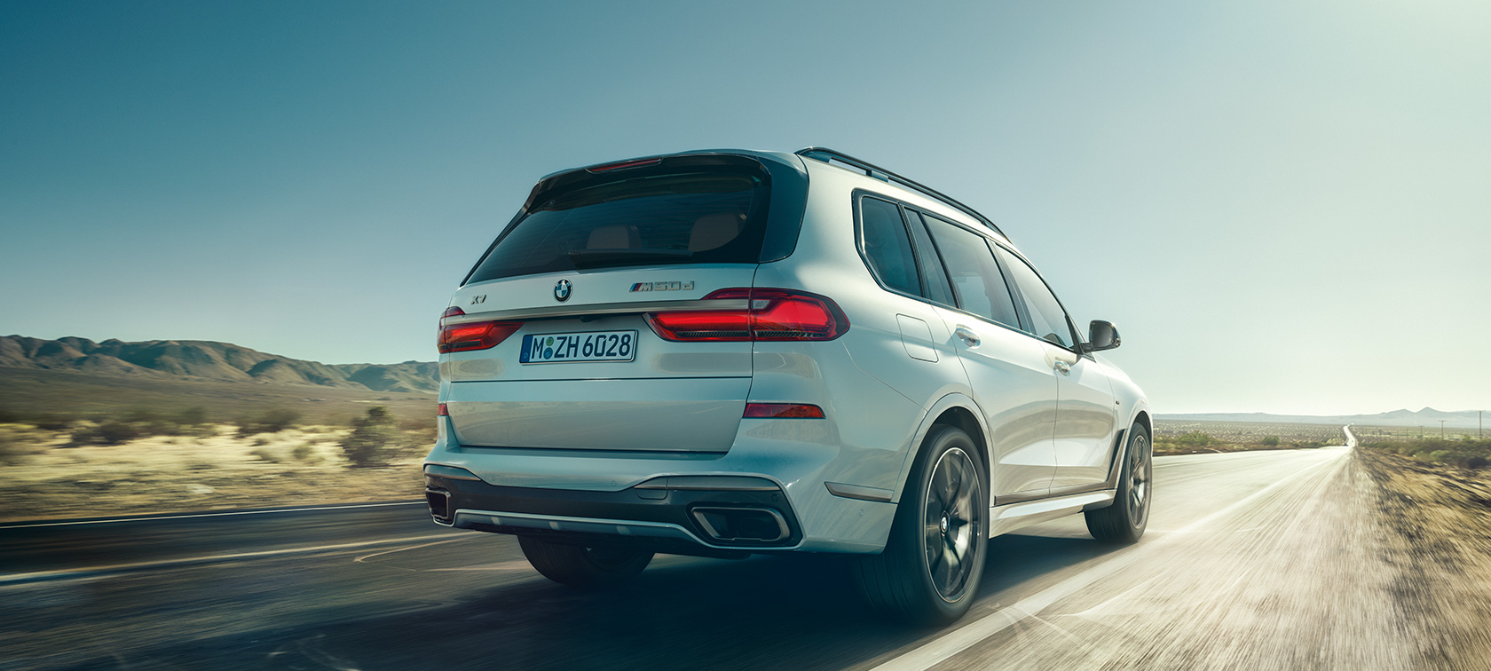 BMW X7 M50d sett bakfra BMW X7 M50d i mineralhvit, i fart på en øde Highway, sett bakfra, G07, 2019