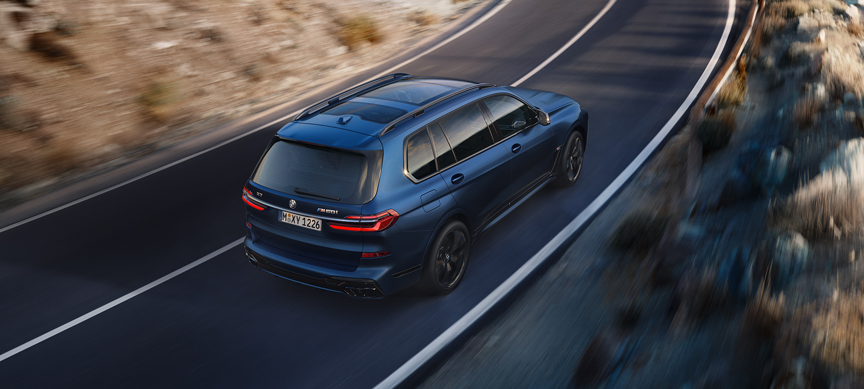 BMW X7 M60i G07 LCI Frozen Marina Bay Blue Sett skrått bakfra i fugleperspektiv kjørende BMW X7 M60i G07 LCI Frozen Marina Bay Blue Sett skrått bakfra i fugleperspektiv kjørende på veien