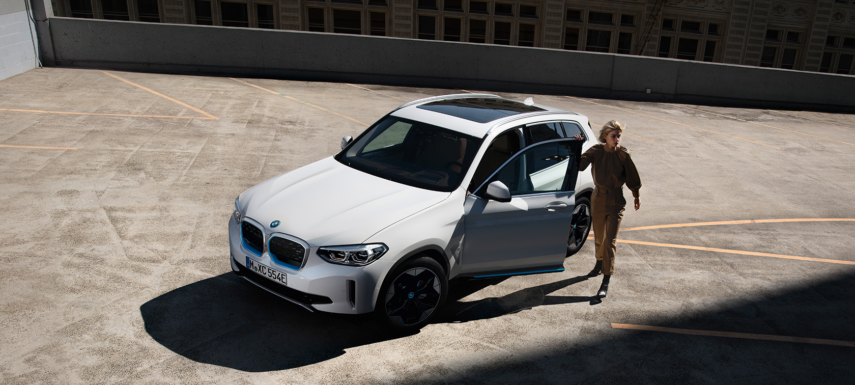 BMW iX3 G08 sett skrått forfra med dame BMW iX3 G08 2020 Mineralhvit metallic sett skrått bakfra med dame i byområde