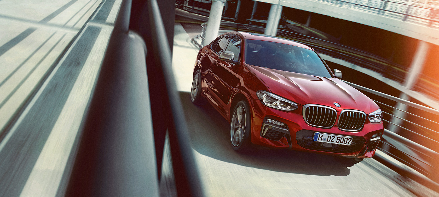 BMW X4 kjørende i parkeringshus BMW X4 G02 2018 Flamencorød med briljanteffekt sett skrått fra siden kjørende i parkeringshus