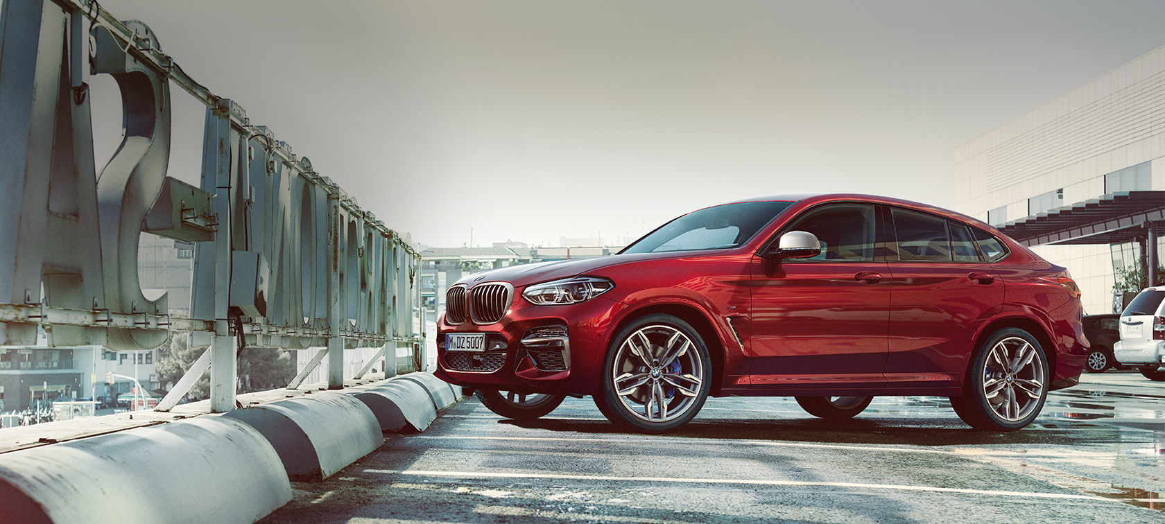 Parkerende sett fra siden BMW X4 BMW X4 M40i G02 2018 Flamencorød med briljanteffekt rød parkert på parkeringsdekke