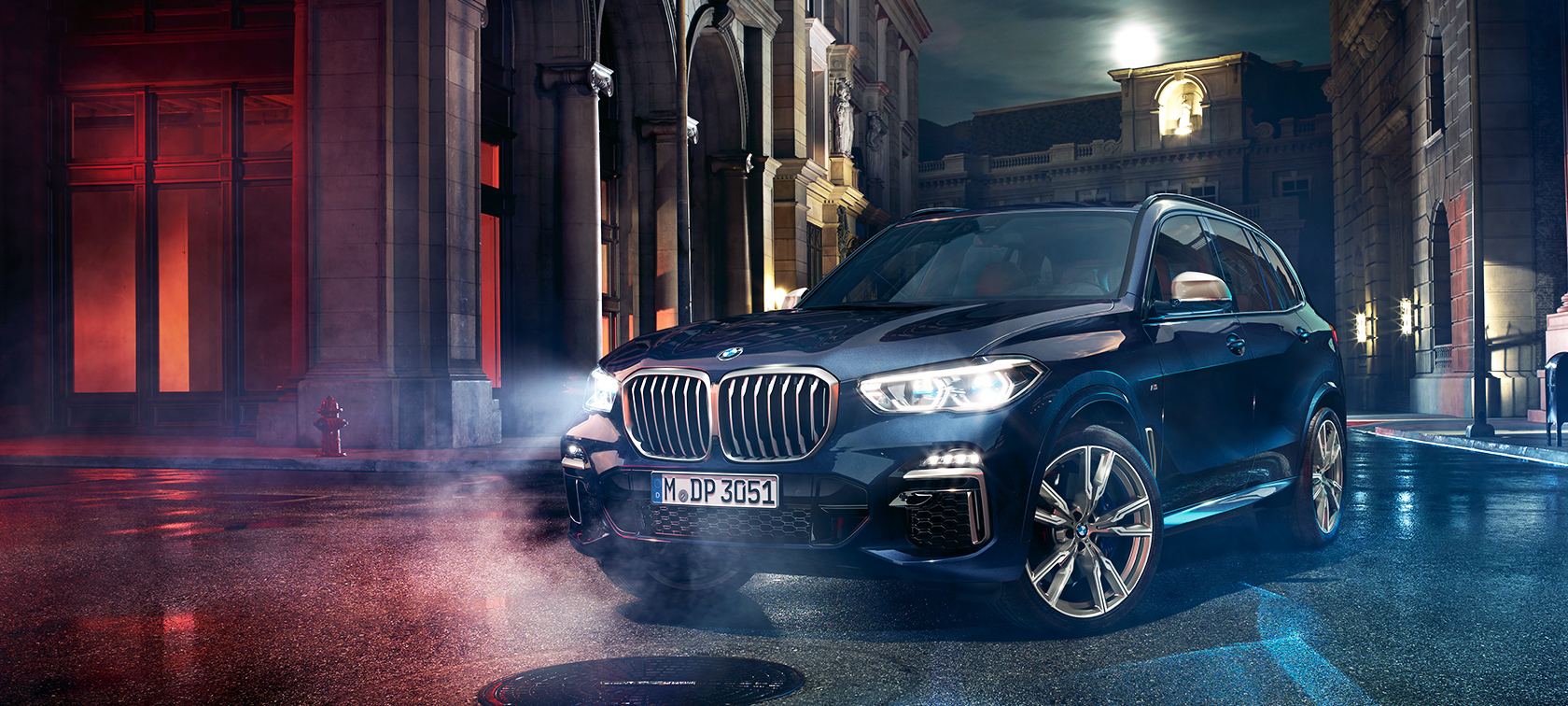 BMW X5 M50d på veien BMW X5 M50d står på veien foran urbant nattlandskap