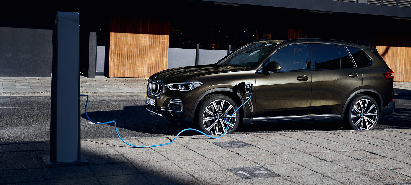 Plug-in-hybrid BMW X5 xDrive45e G05 sett på skrå fra siden Plug-in-hybrid BMW X5 xDrive45e G05 sett på skrå fra siden ved lading