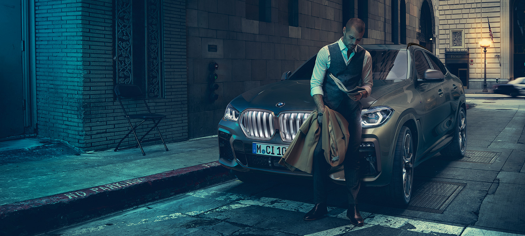 Mann lener seg mot BMW X6. Mann lener seg mot BMW X6 sett fra siden foran bylandskap.