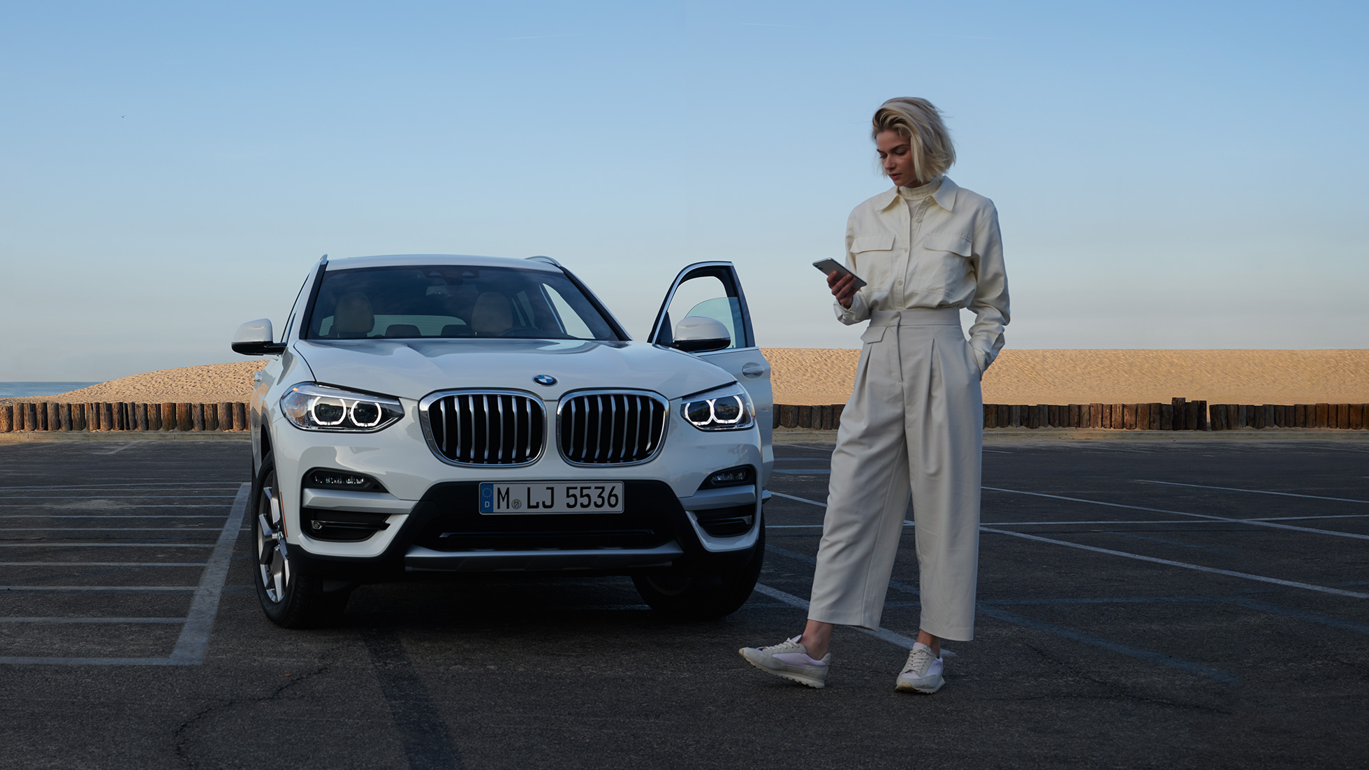 Kvinne bruker My BMW-appen på smarttelefonen Kvinne bruker My BMW-appen fra BMW ConnectedDrive på smarttelefon foran hvit BMW X5