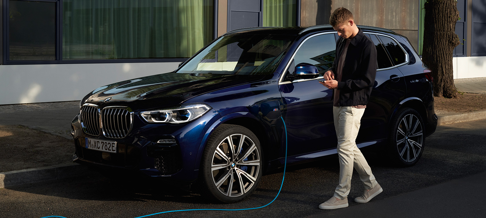 Mann bruker My BMW-appen på smarttelefonen Mann bruker My BMW-app fra BMW ConnectedDrive på smarttelefonen mens hans BMW X5 Plug-in hybrid blir ladet