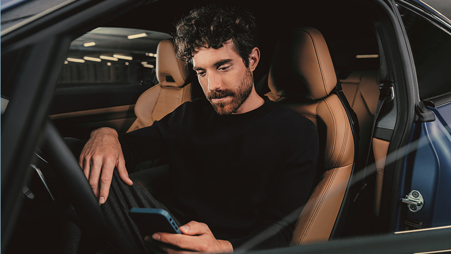 Mann sitter i en BMW Mann sitter i en BMW og ser på sin smarttelefon