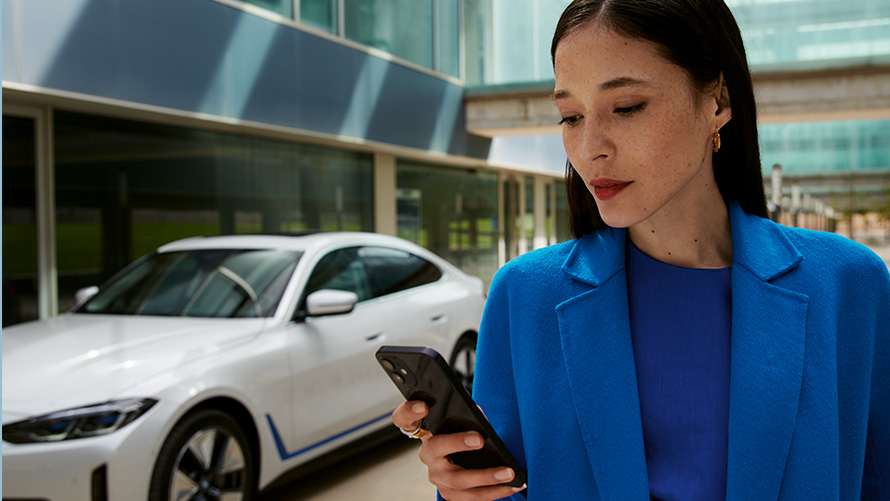 Kvinne stående foran en BMW Kvinne stående foran en BMW og ser på smarttelefonen sin