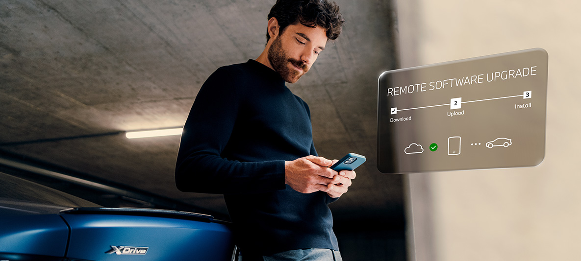 Mann som lener seg mot en BMW hekk og ser på sin smarttelefon Remote Software Upgrade Mann som lener seg mot en BMW hekk og ser på sin smarttelefon