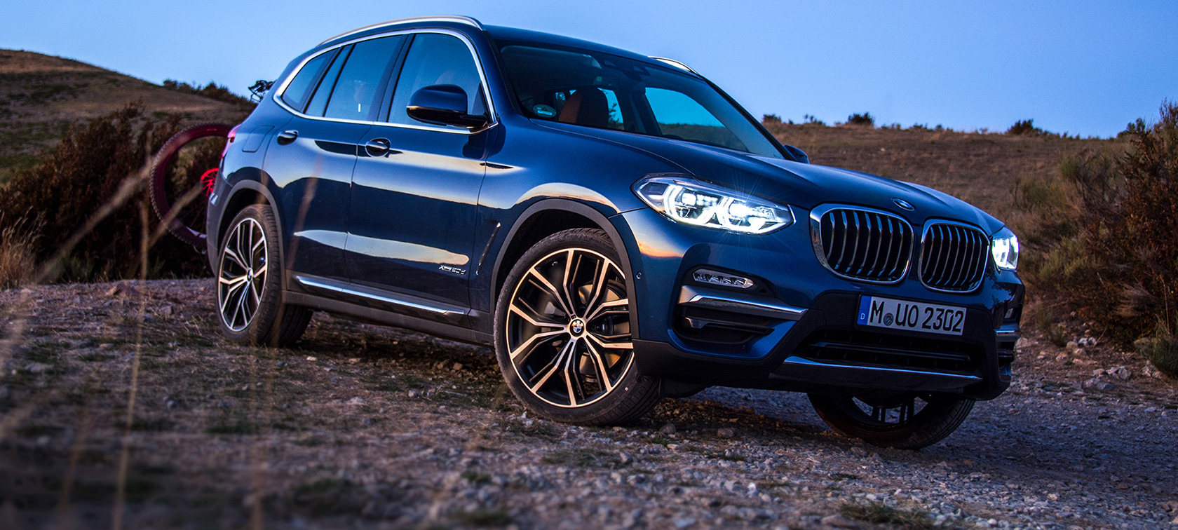 Mørkeblå BMW X3 i terrenget Mørkeblå BMW X3 med hekkmontert sykkelstativ og sykkel står i terrenget